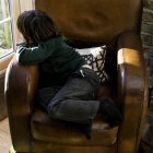 Chico relajándose en silla de brazo después de la escuela - foto de stock