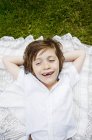 Menino deitado na toalha de mesa na grama com as mãos atrás da cabeça — Fotografia de Stock