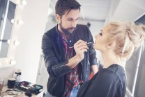 Male make up artist applying lipstick to model for photo shoot — Stock Photo