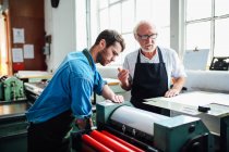Senior Handwerker / Techniker betreut jungen Mann auf Buchdruckmaschine in Buchkunstwerkstatt — Stockfoto
