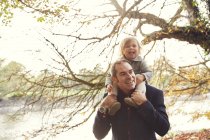 Father carrying daughter on shoulders in autumn park — Stock Photo