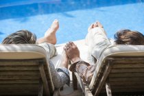 Visão traseira do casal romântico masculino de mãos dadas à beira da piscina — Fotografia de Stock