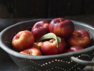 Fresh organic donut nectarines with leaf in colander — Stock Photo