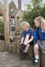 Schulmädchen beobachtet Jungen beim Binden von Schnürsenkeln am Holzzaun — Stockfoto