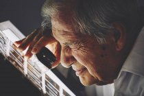 Senior man looking at sheet of film slides with magnifier — Stock Photo