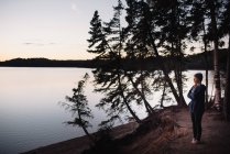 Взрослая женщина, стоящая у озера, глядя на вид — стоковое фото