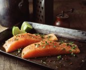 Raw salmon with lime wedges, herbs and seasoning on baking tray — Stock Photo