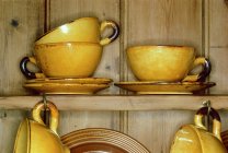 Yellow cups and saucers in cupboard — Stock Photo