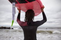 Visão traseira de surfista feminina carregando prancha na cabeça em Rockaway Beach, Nova York, EUA — Fotografia de Stock