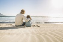 Батько й син сидять на пляжі переглядає геть Переглянути — стокове фото