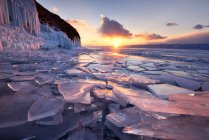 Зламаний лід на березі озера з хмарним небом заходу сонця — стокове фото