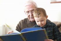 Старший чоловік читає книгу онуку — стокове фото