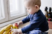 Дитячий хлопчик сидить на кухонній лічильнику, граючи з мискою фруктів — стокове фото