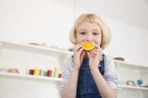 Retrato de bonito menina no cozinha segurando laranja fatia para ela boca — Fotografia de Stock