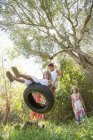 Vista de ángulo bajo de cuatro niñas jugando en árbol de neumáticos columpio en el jardín - foto de stock
