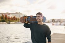 Молодой человек, гуляющий у реки с скейтбордом, Бристоль, Великобритания — стоковое фото