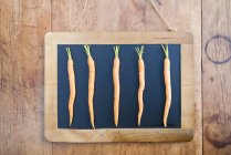 Cinco zanahorias en el tablero negro, naturaleza muerta - foto de stock
