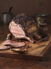 Lomo de cerdo con corteza de pimienta y glaseado en rodajas sobre tabla de madera - foto de stock