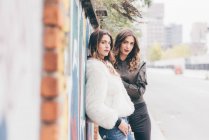 Portrait of twin sisters, outdoors, leaning against wall — Stock Photo