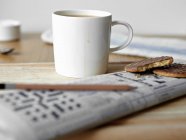 Tasse à café avec biscuits et mots croisés sur la table — Photo de stock