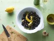 Top view of bowl of black olives with lemon peel on table — Stock Photo