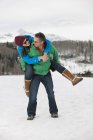 Uomo maturo che trasporta giovane donna sulla schiena nella neve — Foto stock