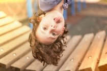 Menina no playground pendurado de cabeça para baixo olhando para a câmera saindo da língua — Fotografia de Stock