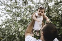 Portrait of baby girl held up by her father in garden — Stock Photo