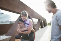 Two women giving piggyback on urban footbridge with male personal trainer — Stock Photo
