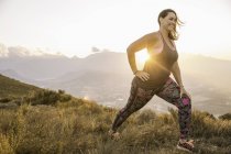 Side view of plus size woman wearing sports clothing on mountain, lunging at sunrise — Stock Photo