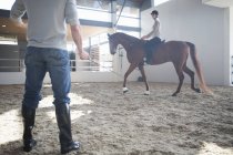 Équitation féminine avec instructeur dans le paddock intérieur — Photo de stock