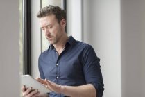 Hombre usando tableta digital por ventana de oficina - foto de stock