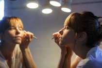 Середня доросла жінка застосовує підводку для очей у дзеркалі ванної кімнати — стокове фото