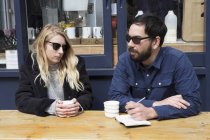 Пара сидящих за столом кафе на тротуаре, записывающих в записную книжку — стоковое фото