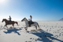 2 people riding horses in the sand — Stock Photo