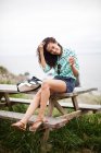 Young woman sitting on picnic table smiling, portrait — Stock Photo