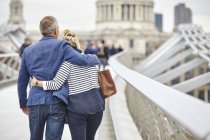 Rear view of mature dating couple  crossing Millennium Bridge, London, UK — Stock Photo