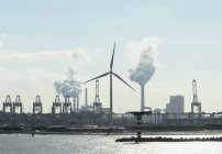 Vista silueta de turbina eólica, terminal de contenedores y central eléctrica de carbón en el puerto de Rotterdam, Países Bajos - foto de stock