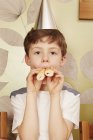 Boy wearing party hat with party food in mouth — Stock Photo