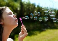 Дівчина дме бульбашки на відкритому повітрі, фокус на передньому плані — стокове фото