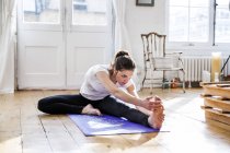 Молодая женщина практикует йогу, трогает пальцы ног в квартире — стоковое фото