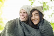 Casal jovem usando chapéus de malha envolto em cobertor — Fotografia de Stock
