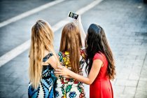 Rear view of three young women taking selfie with smartphone, Cagliari, Sardinia, Italy — Stock Photo