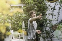 Молодий чоловік кидає м'яч у сад — стокове фото