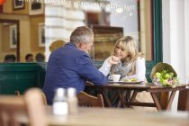 Mature dating couple chatting together at sidewalk cafe table — Stock Photo