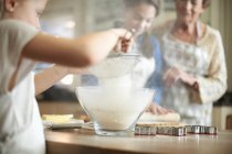 Senior woman and granddaughters sifting flour for Christmas tree cookies — Stock Photo