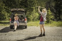 Young woman photographing teenage girl hiker holding up walking stick on rural road, Red Lodge, Montana, USA — Stock Photo