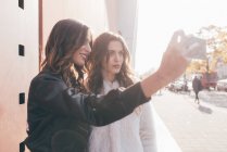 Twin sisters, outdoors, taking selfie, using smartphone — Stock Photo