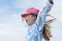 Chica con gorra rosa con los brazos levantados en el viento - foto de stock