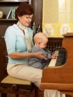 Abuela tocando el piano con bebé - foto de stock